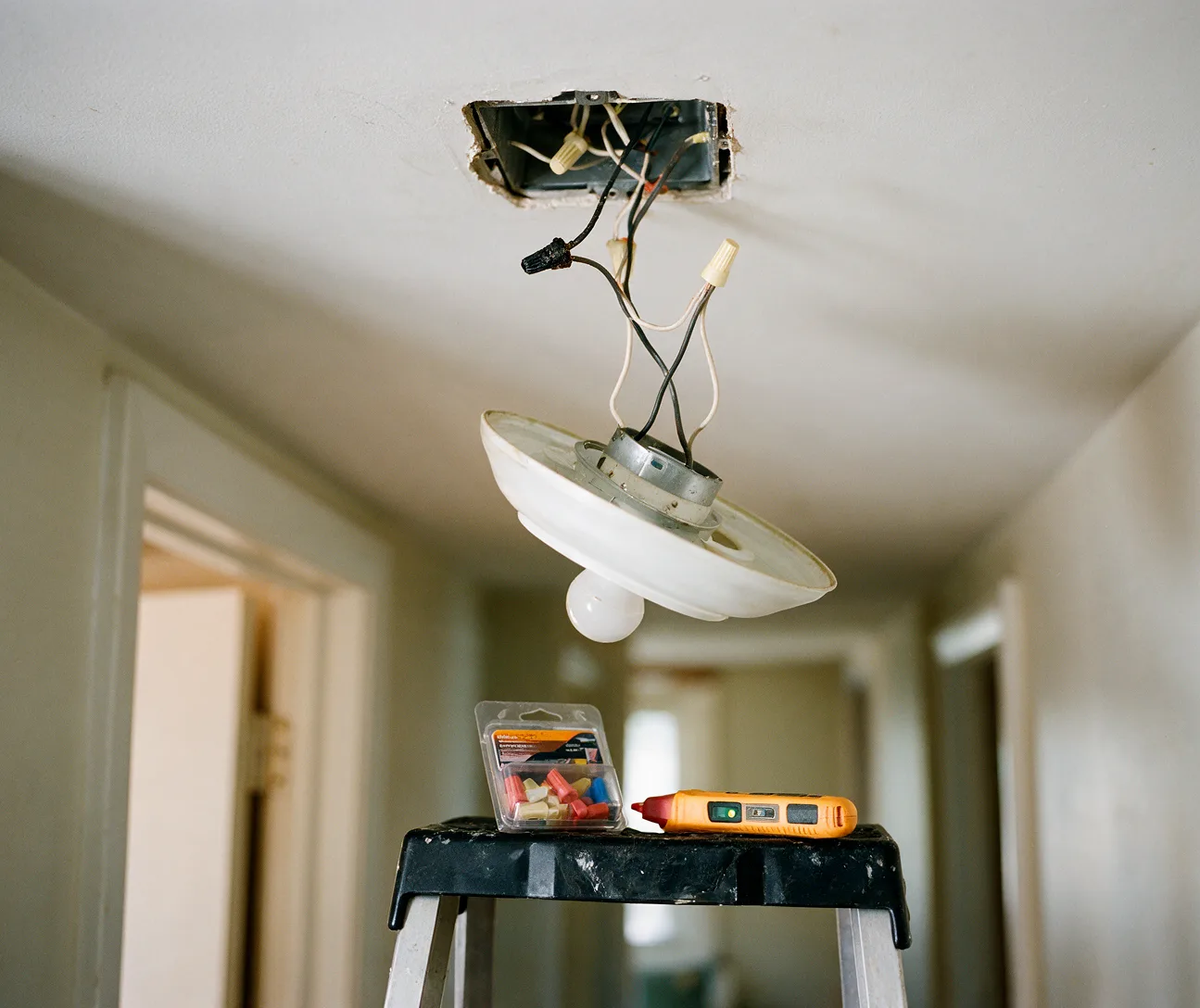 A ceiling light fixture hanging from an open junction box during a repair